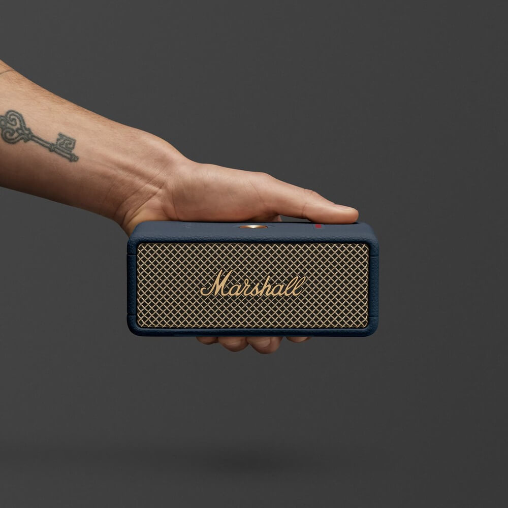 Marshall Emberton III Midnight Blue в руке &mdash; демонстрация компактности и логотипа на золотистой сетке