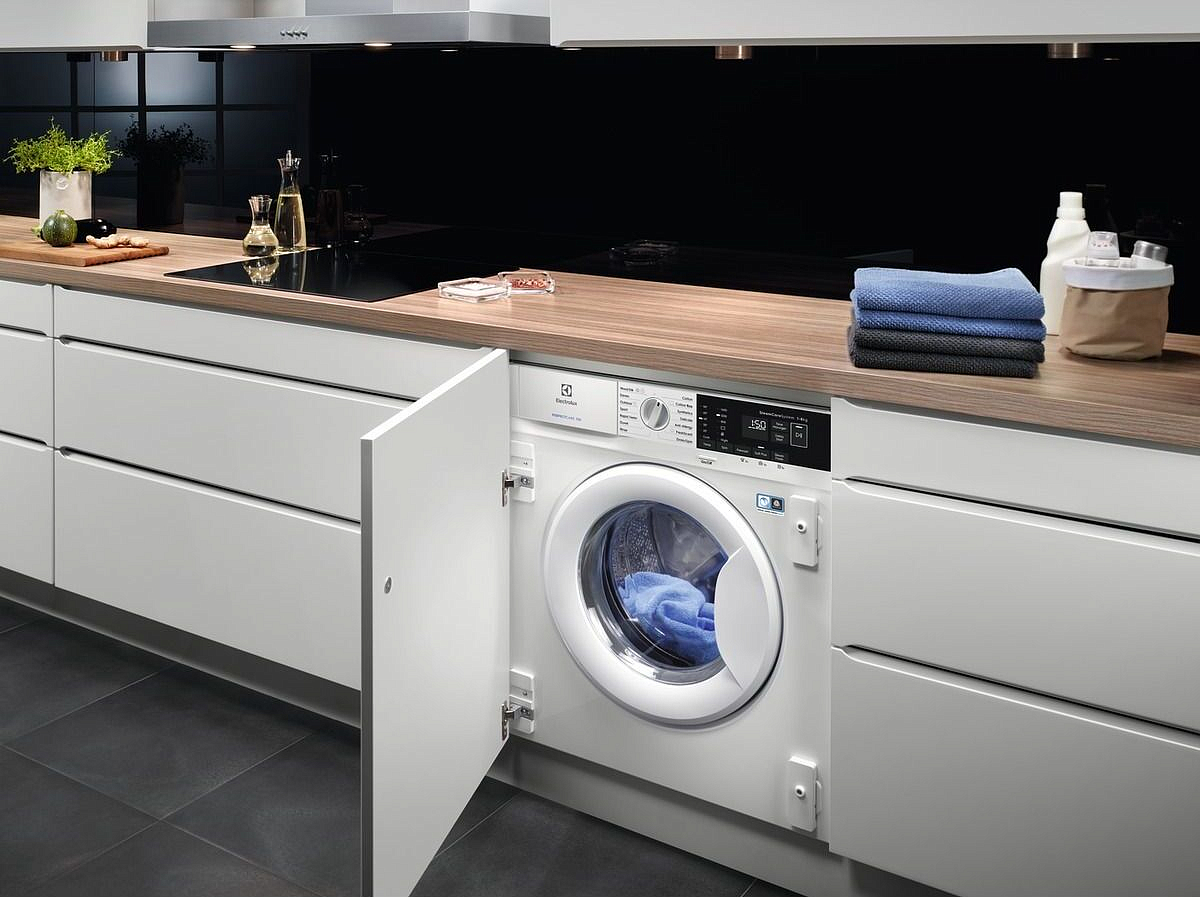 Electrolux EWN7F447WI встраиваемая стиральная машина в кухонном интерьере с открытой дверцей и голубым бельём в барабане